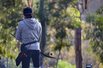 View from behind of a young men practicing archery at an outdoor field.