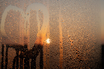 Obraz premium condensation on the window glass at sunset, wet glass with lots of water droplets on the background of an orange sky