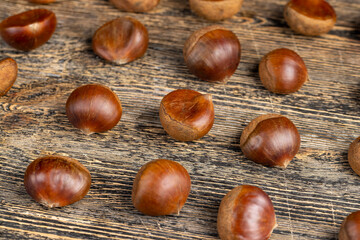a hard chestnut fruit in a brown shell on a wooden table, a group of raw fruits of chestnut with a hard shell of brown color