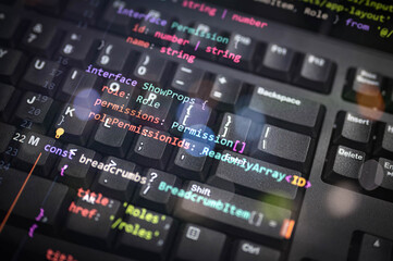 Colorful programming interface code overlay on black keyboard, showcasing software architecture, permissions, and user role systems in modern web development and secure application environments.