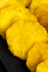 ripe bright yellow pineapple fruits on a black slate board, cut into rings and dried yellow clean slices of ripe pineapple for long-term storage and used as a sweet