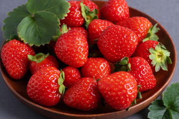 Freshly picked strawberries arranged neatly on a brown wooden plate with green leaves nearby