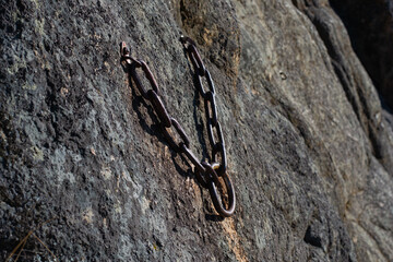 rustic metal chain anchor fixed into rugged rock surface, providing secure point for climbing equipment, symbolizing safety, adventure, and outdoor recreation. close up.