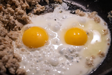 Cooking fried eggs with minced meat for breakfast. Cooking scrambled eggs for quick, nutritious breakfast before work. The concept of food consumption. Frying chicken eggs in a black skillet. 
