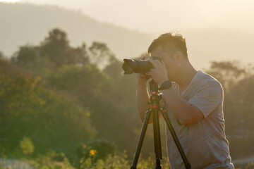 A male traveler photographs a breathtaking natural landscape during the golden hour of evening.