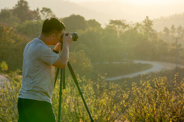 A male traveler photographs a breathtaking natural landscape during the golden hour of evening.