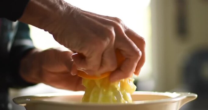 Close-up of a person's hands squeezing a fresh citrus fruit on a manual juicer into a bowl.