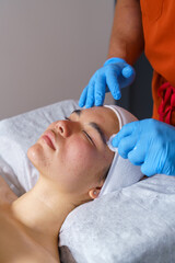 Young Japanese woman receiving professional acne facial treatment, beautician applying solution to her face © Javier