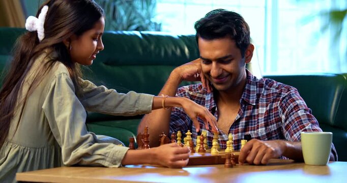 Playing chess together, Indian father and daughter sitting at table at home, Asian dad bonding with young girl over board game, family quality time, learning strategy, concentration, and fun
