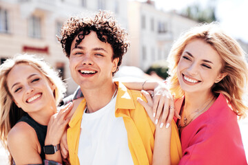 Group of young three stylish friends posing in the street. Fashion man and two cute female dressed in casual summer clothes. Smiling models having fun. Cheerful women and guy outdoors