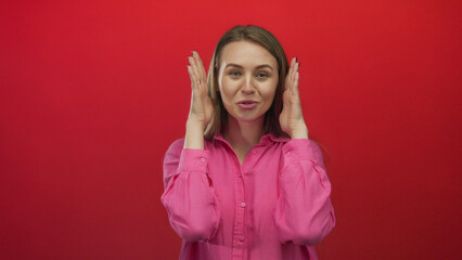 Woman posing playfully in a pink shirt against a vibrant red wall, exuding happiness and charm, creating a lively yet isolated appeal with her expressive gestures and youthful radiance.