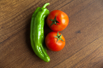 Fresh, tasty organic vegetables, red tomato and green pepper, isolated on brown wood cutting board