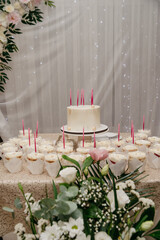 In a restaurant, on a banquet table, there is a white cake with candles in it, surrounded by a large number of cupcakes for a wedding or birthday celebration