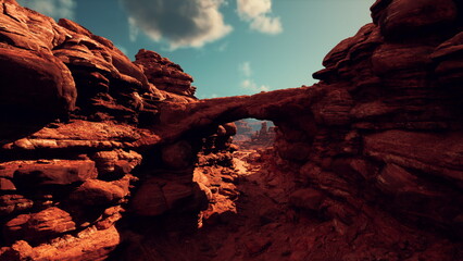 A stunning natural arch rises above the rocky landscape, bathed in warm sunlight. The red rocks create a striking contrast against the deep blue sky, showcasing natures beauty.