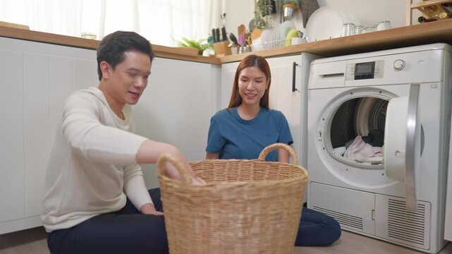 Attractive couple put dirty clothes to washing machine in house together. 