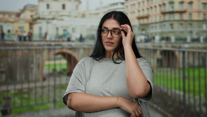 Fototapeta premium Woman standing confidently near historic roman ruins, wearing glasses and casual clothing, showcasing plus size beauty in a vibrant cityscape with ancient architecture in rome.