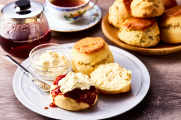 紅茶とともに楽しむアフタヌーンティーのスコーン。クロテッドクリームとジャムを添えて味わう伝統的な英国風ティータイムの一場面。ティーポットやカップと共に並べられたスコーンは、洋菓子、デザート、カフェ、休日のひとときを表現する素材写真として利用可能。