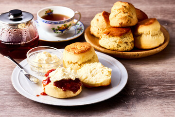 紅茶とともに楽しむアフタヌーンティーのスコーン。クロテッドクリームとジャムを添えて味わう伝統的な英国風ティータイムの一場面。ティーポットやカップと共に並べられたスコーンは、洋菓子、デザート、カフェ、休日のひとときを表現する素材写真として利用可能。