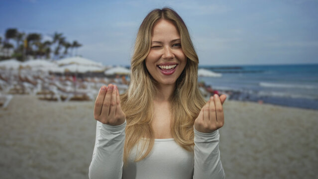 Blonde woman hands showing money sign gesture at beach; wealth prosperity playfulness spending vacation.