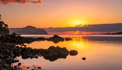 Vibrant Sunset Over Rocky Shoreline With Mountain Silhouette and Golden Reflections in Calm Water at Dusk
