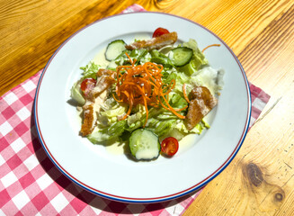 A salad with lettuce, carrots, and cucumbers on a white plate