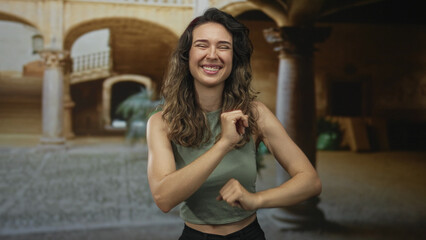 Fototapeta premium Woman with exposed midriff swaying and dancing with raised fists in sunlit cobblestone street; joy.