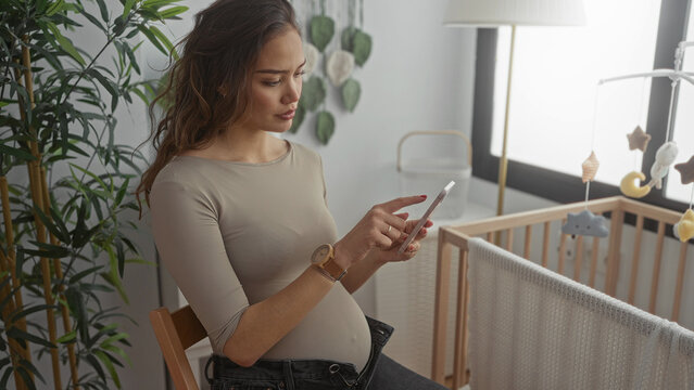 Pregnant woman using smartphone in stylish baby room with crib and plants, showcasing modern motherhood and preparation. - Powered by Adobe