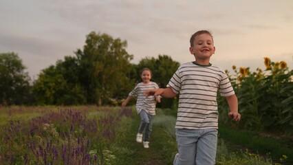 Fototapeta premium Happy children running in a summer field, Smiling boy and girl playing outdoors, Kids enjoying nature and fresh air, Siblings having fun together at sunset, Carefree childhood moments in the