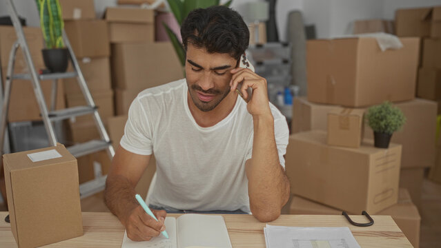 Man writing with pen in notebook and holding phone to ear in a building; planning productivity focus. - Powered by Adobe