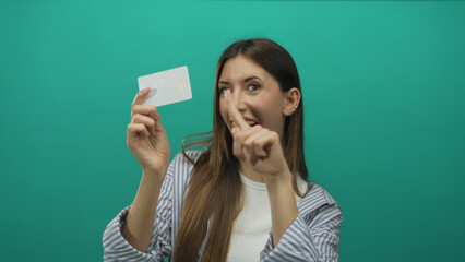 Young hispanic woman smiling holds creditcard and points finger to card in studio; approval confidence.