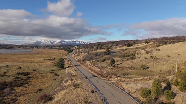 Provincial Route 71 crossing the vast Patagonian plains in Chubut Province, Argentina, with distant Andres snow-capped mountain ridge under a partly cloudy sky on a crisp, clear morning drone shot