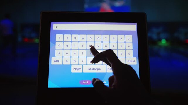 Closeup of hand typing player name Olivia on bowling touchscreen before match