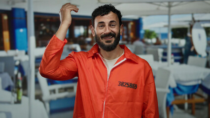 Fototapeta premium Hispanic man in prison jumpsuit smiling in a restaurant setting, surrounded by tables, creating a striking contrast between his attire and the casual dining background.