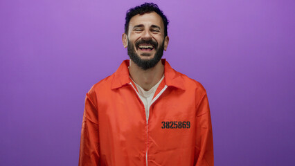Hispanic man with beard in orange prison jumpsuit stands against a purple background, displaying a range of emotions.