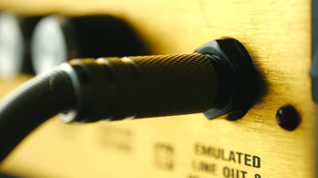 Close up guitarist inserting 14 inch instrument jack into emulated line out golden guitar amplifier, preparing for recording session, live performance. Guitarist plugging audio jack cable in amplifier