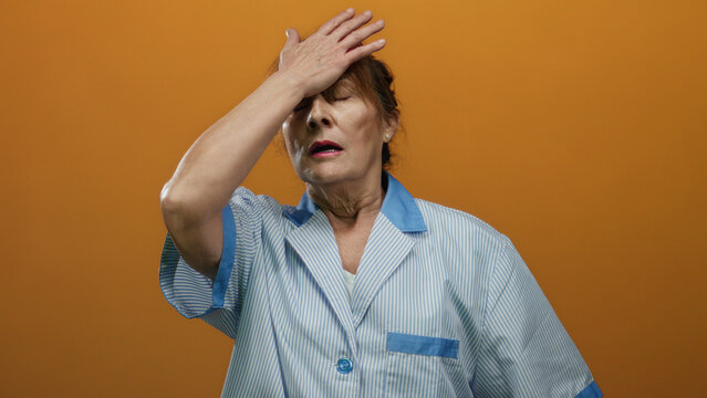 Woman in uniform cleaning with orange background looking tired and frustrated, showcasing senior hispanic cleaner isolated in vibrant setting.