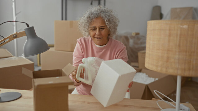 Woman packing in new home with boxes around, wearing pink sweater in cozy living room setting.