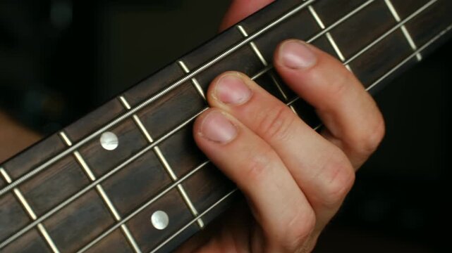 Skilled bass player fingers pressing strings on fretboard, performing bass line with precision during musical performance or practice session. Musician hand playing notes on bass guitar fretboard