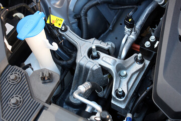 Close-up of vehicles top engine mount showing metal components, bolts, and wiring under hood of electric vehicle. Engine mount new car. Engine parts under the hood of the car.