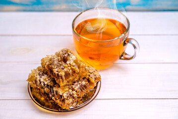 honey in honeycombs and a mug of tea on a whitewooden background
