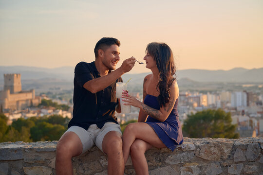 Couple enjoying romantic date feeding iced coffee drinks at sunset