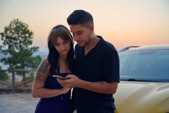 Young couple using smartphone together during sunset trip
