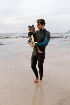 Father and daughter in wetsuits on the beach