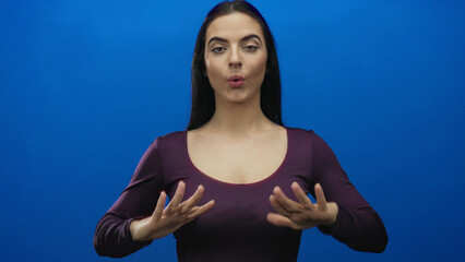 Woman gestures calming with hands against vivid blue wall, expressing serenity and relaxation,...