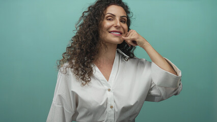 Woman using finger phone gesture in studio with turquoise background; communication connection friendliness.