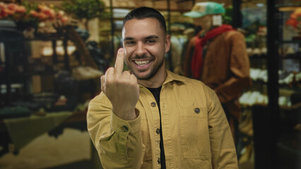 Man shows middle finger gesture in a clothing store building while wearing a yellow jacket;...