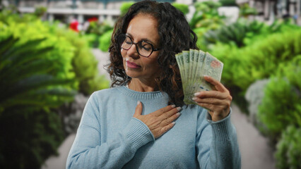 Woman in garden holds argentine pesos to chest, symbolizing pride and prosperity outdoors.