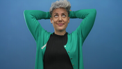 Short haired woman wearing green cardigan with hands behind head in studio; calm contentment...
