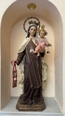 Our Lady of Mount Carmel Statue: A serene statue of Our Lady of Mount Carmel cradles a child, the depiction radiates faith and peace. The setting reveals a sacred niche.