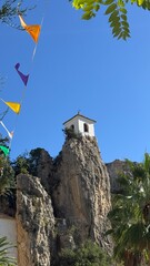 Scenic View: A small, white chapel perched atop a rugged rock formation against a brilliant blue sky. The image captures a serene moment, embodying the timeless beauty of nature and architecture.